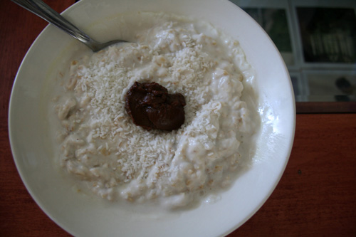 Refreshing bowl of muesli with coconut milk, shreds, vanilla, and a blob of Cacao Bliss.